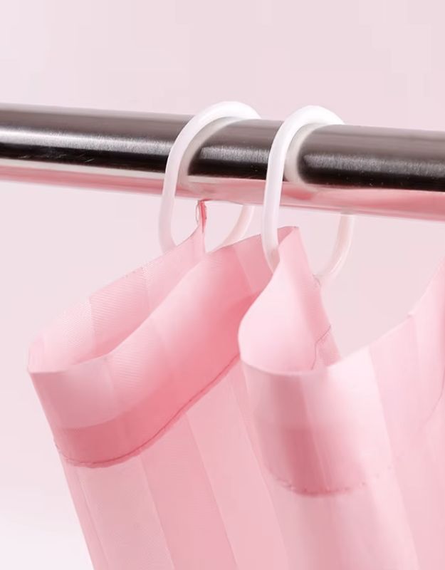 Closeup of pink striped shower curtain hanging on rod with hooks.